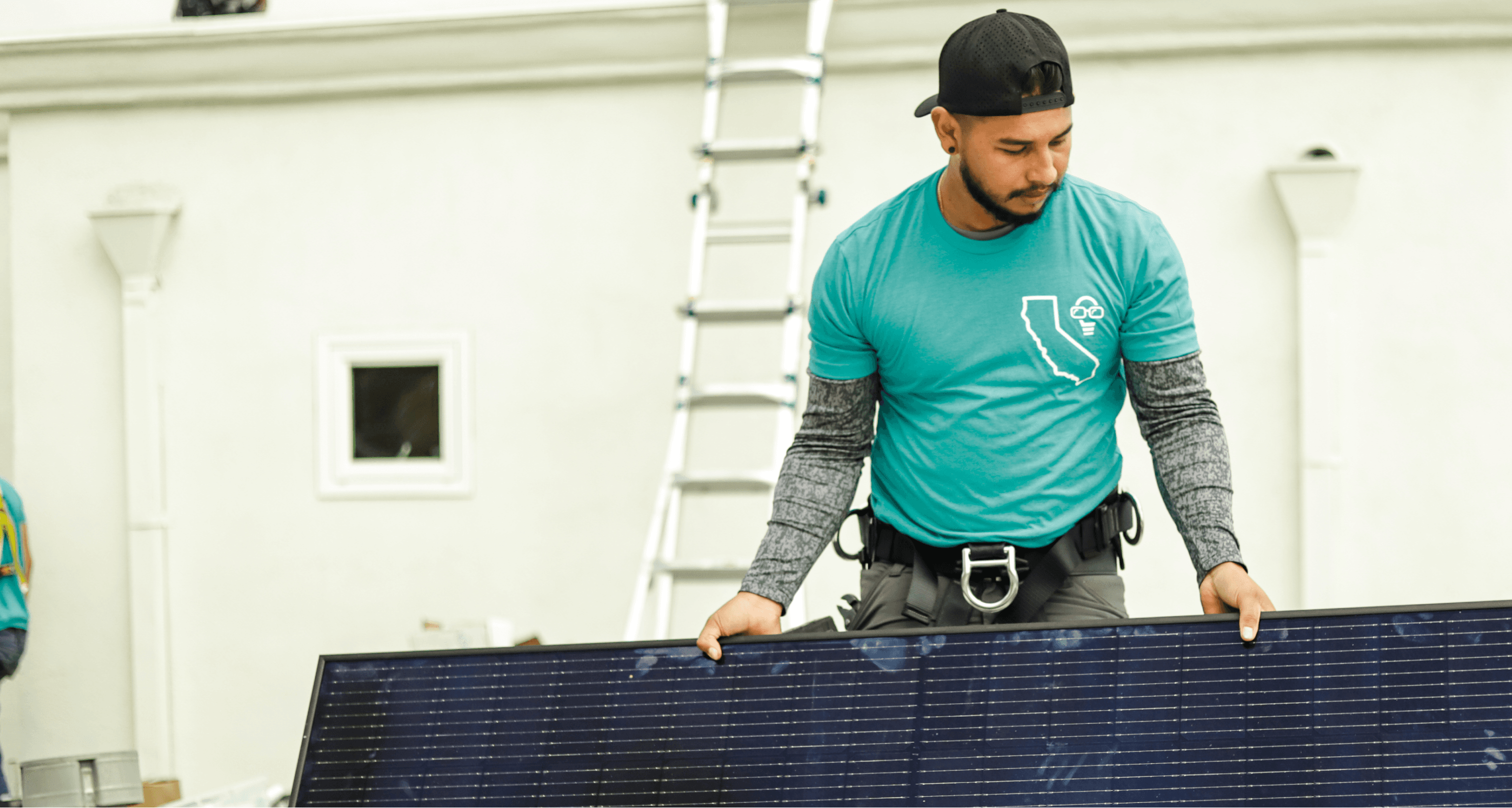 A man in a blue shirt holding a solar panel outdoors on a sunny day.