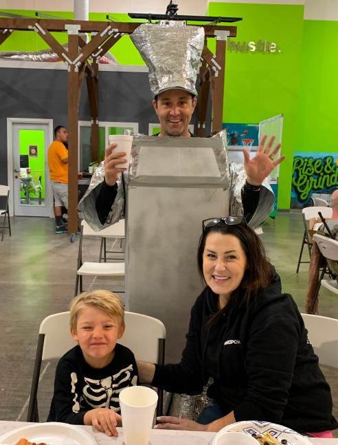 A man and woman in tin costumes pose for a photo with a child at a costume party.